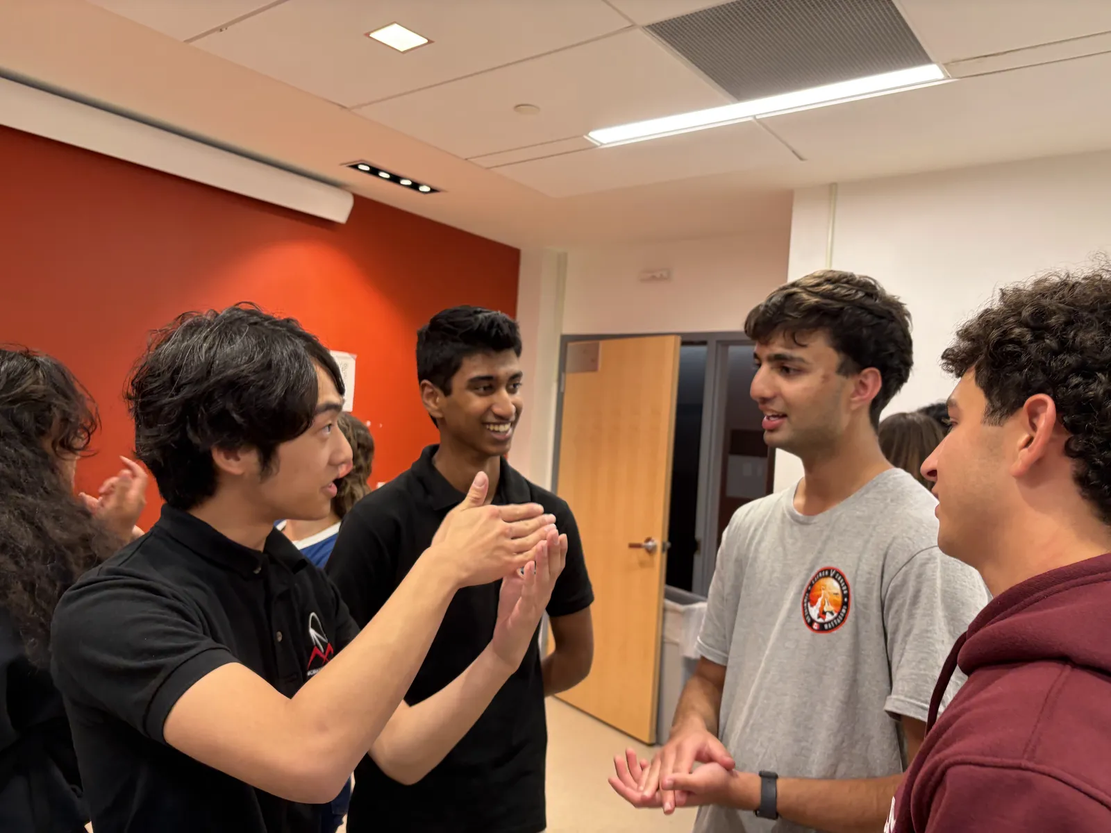 Two team members in black McMaster Rocketry polos talking with two students at the fall 2026 info night.