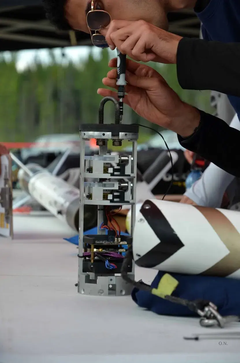 A team member fastens hardware on the Magpie stack beside the Osiris nose cone at the range.