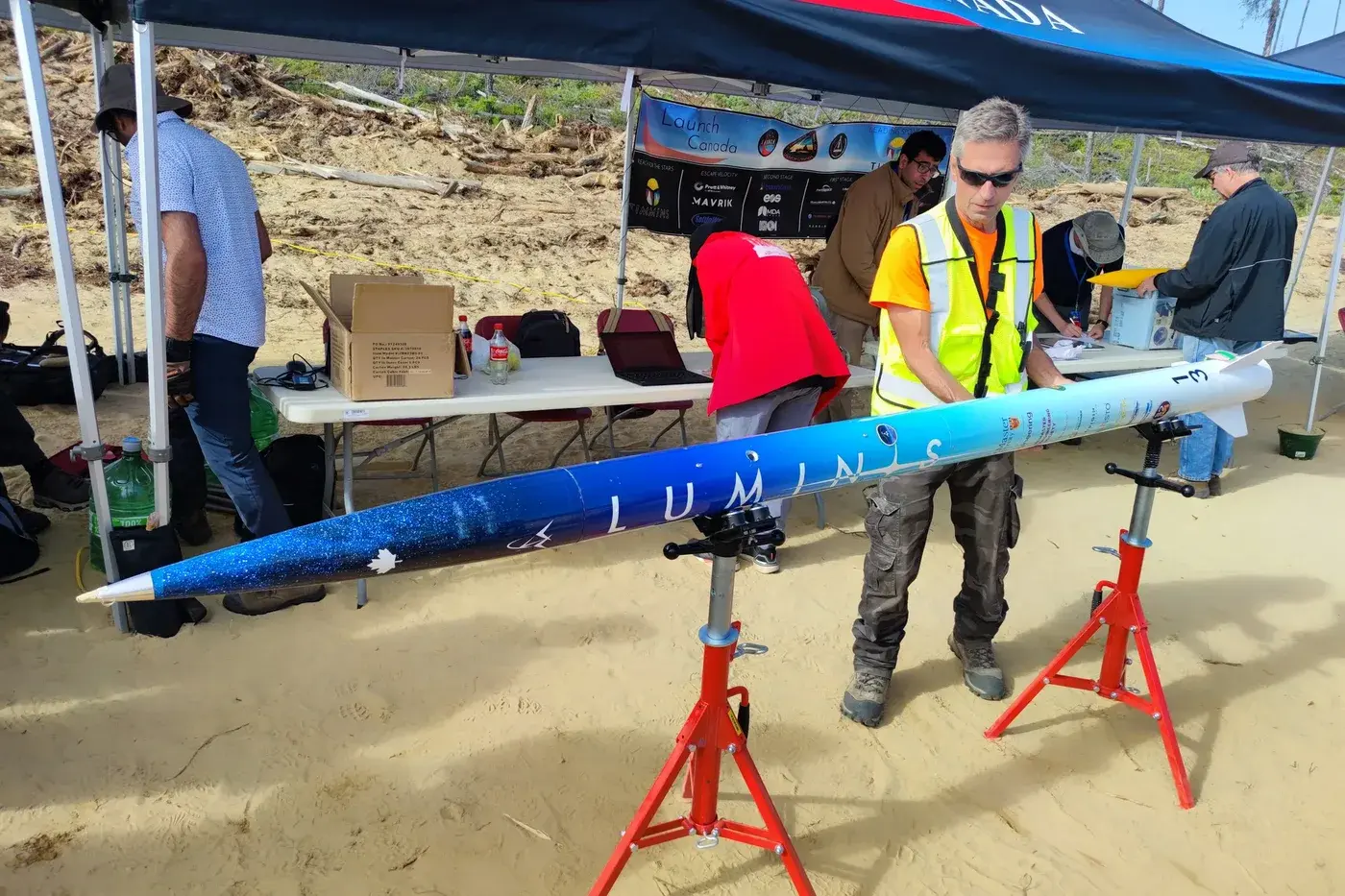 Luminis V2 lies horizontal under the Launch Canada tent, full airframe from nose to fins, bib 13 on the tail.